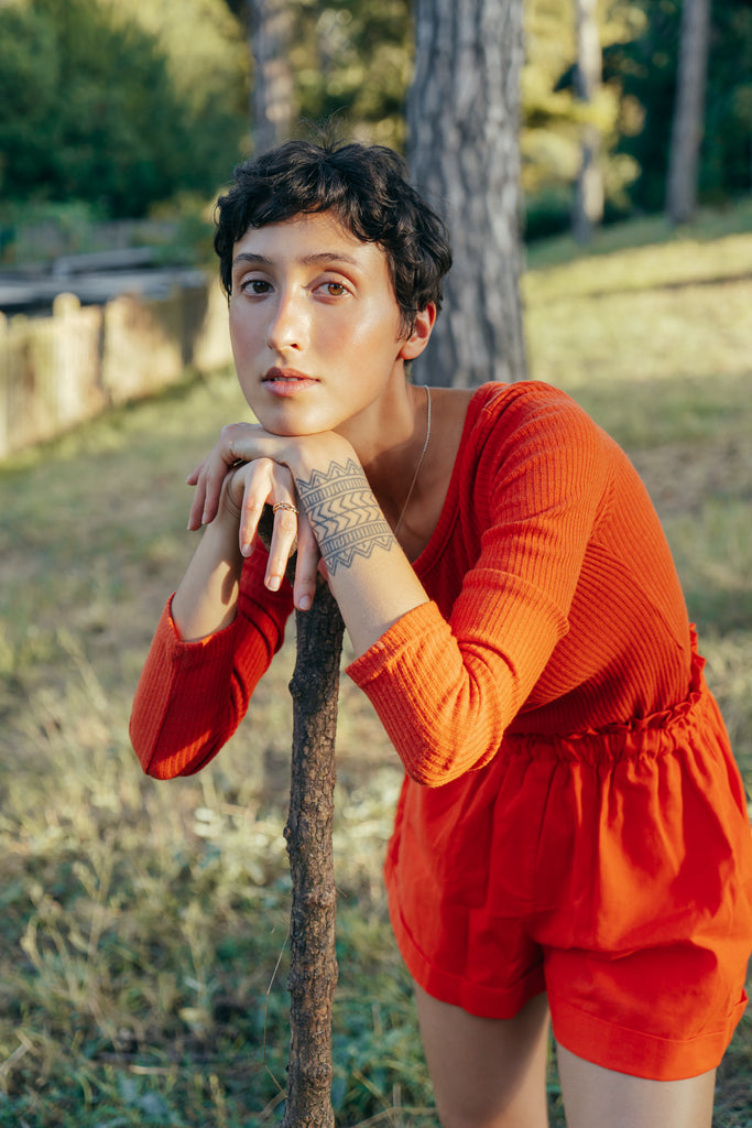 La modelo lleva un twin set en color naranja, hecho con tejidos de stock mientras posa en el bosque